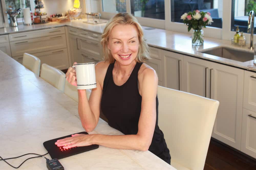 A woman drinking coffee in the kitchen while using red light therapy pads for hand pain